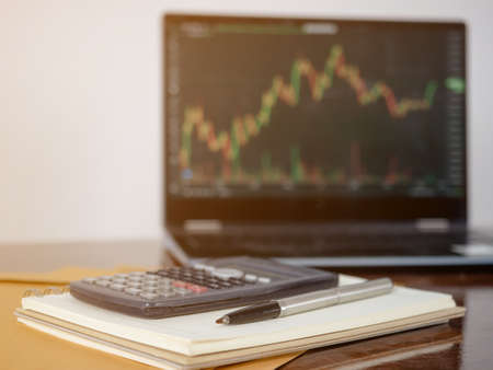 Close-up pen on page notebook front of laptop invisment graph backgroundの写真素材