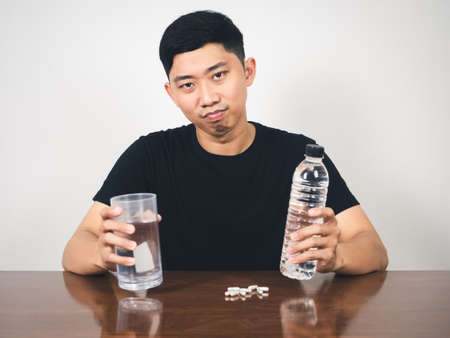 Young man hold water with pill medicine on table looking at cameraの写真素材