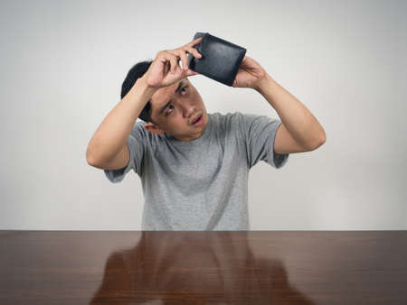 Young man sitting and hold wallet finding money feels sad