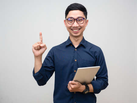 Young businessman cheerful smile hold tablet point finger up isolatedの写真素材
