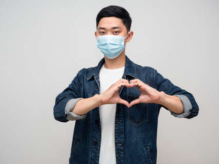 Positive young man jeans shirt wear medical mask show hand heart sign isolated