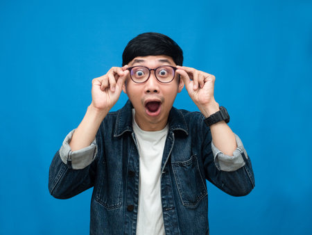Portrait man jeans shirt feels amazed looking at camera blue backgroundの写真素材