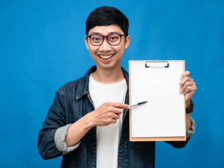 Young businessman gentle smile show checklist board blue backgroundの写真素材