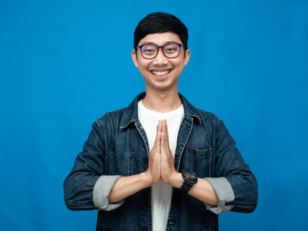 Asian man jeans shirt gentle smile gesture respect hand blue backgroundの写真素材