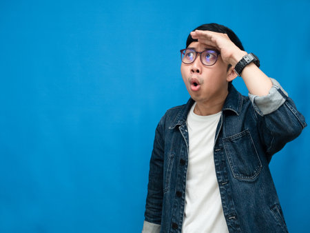 Asian man jeans shirt hand at head feels amazed blue backgroundの写真素材