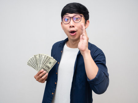 Young asian man glasses hold money gesture whisper to you isolatedの写真素材