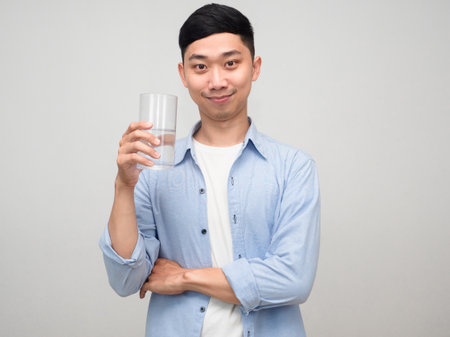 Handsome asian man blue shirt hold glass of water gentle smile isolatedの写真素材
