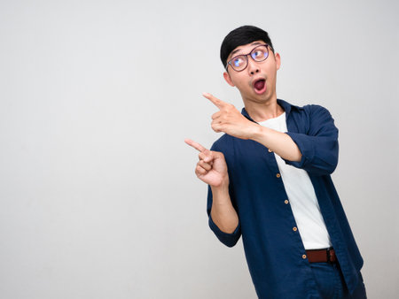 Positive asian man wear glasses turn around to gesture point finger isolatedの写真素材