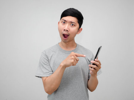 Young asian man hold mobile phone feels amazed point finger at mobile phone