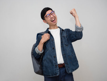 Positive asian man jeans shirt wear glasses carry bag show fist up happy with successful isolatedの写真素材