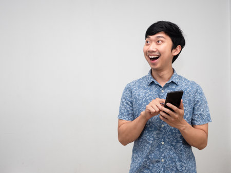 Positive asian man blue shirt using mobile phone with happiness smile looking at copy space isolatedの写真素材
