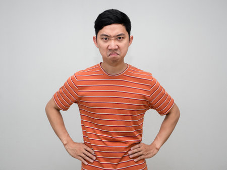 Asian man striped shirt stand hand at waist feels angry looking at you isolatedの写真素材