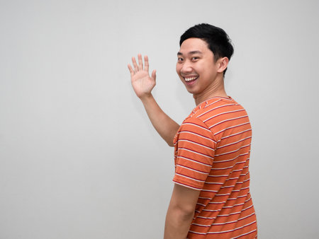 Positive man orange striped shirt cheerful smile turn around to show hand hello isolatedの写真素材