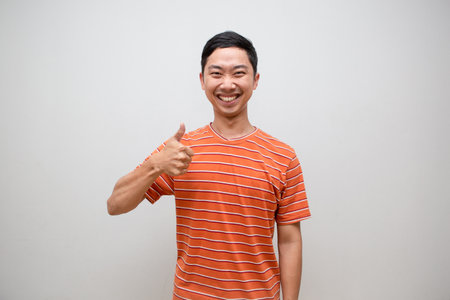 Cheerful asian man orange shirt show thumb up with happy smile with successful isolatedの写真素材