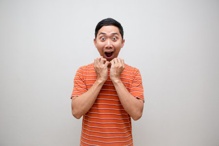 Asian man orange shirt feels excited shocked face isolatedの写真素材