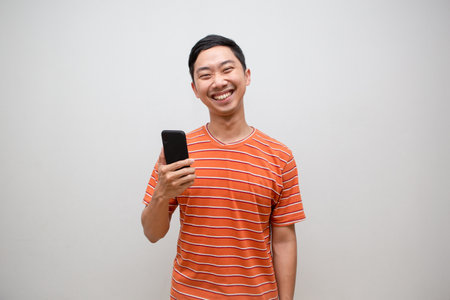 ASian man orange shirt cheerful holding smartphone with happy smile isolatedの写真素材
