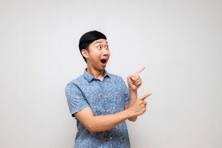 Positive cheerful man blue shirt amazed gesture point finger isolatedの写真素材