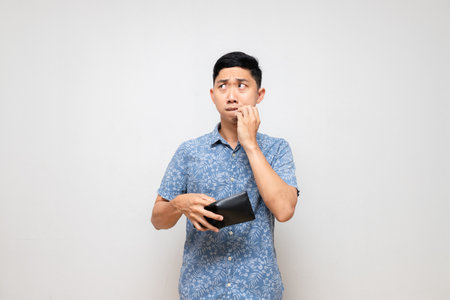 Asian poor man blue shirt holding empty wallet in hand feels sad and worried isolatedの写真素材