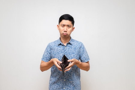 Asian poor man blue shirt holding empty wallet in hand feels sad and worried isolatedの写真素材
