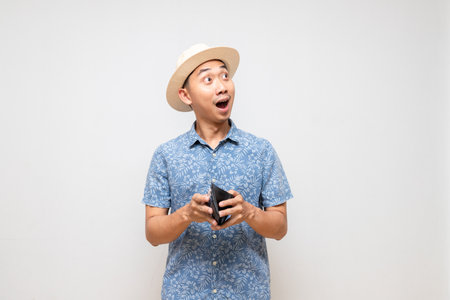 Positive asian man blue shirt wear hat holding wallet amazed isolatedの写真素材