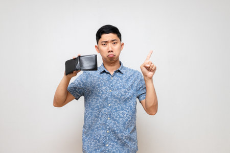 Asian poor man blue shirt feels sad shake his wallet no money and point finger isolatedの写真素材