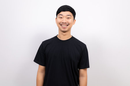 Young Thai man black shirt cheerful with happy smile look at camera crop half body portrait on isolated whiteの写真素材