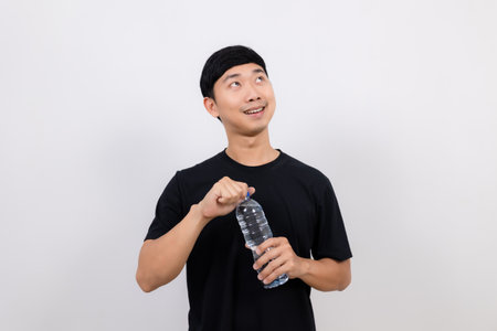 Positive asian man black shirt gesture open water bottle with happy smile look up at space isolatedの写真素材