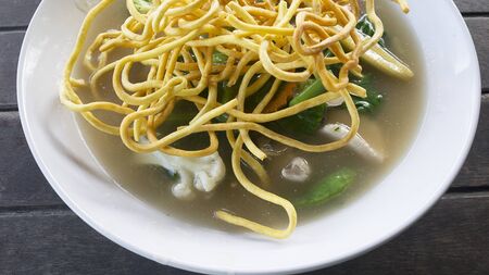 Fried rice noodles topped with vegetable and mushroom in white plate on the dark wood table