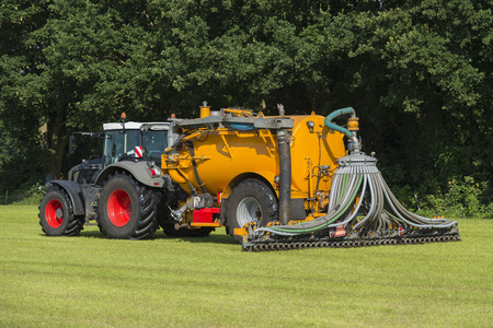 injecting manure in a pasture with a green tractor and yellow vulture tank car in the summer