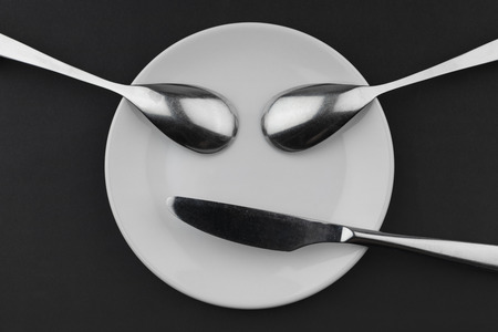 Conceptual face of a ceramic board two metal spoons and a knifeの写真素材