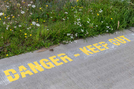 Text Danger Keep Out nearby a beautiful green strip of plants at an airportの写真素材