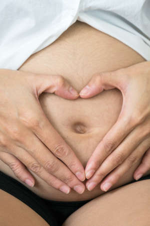 Closeup  of pregnant woman with heart shaped hands on belly's mothers