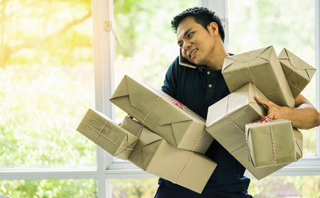 Start up Small and Medium Enterprise SME Concept. Businessman working at home office using mobile and holding packaging box deliveryの写真素材