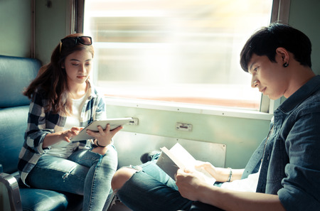 Young couple reading book and using tablet on thr trainの写真素材
