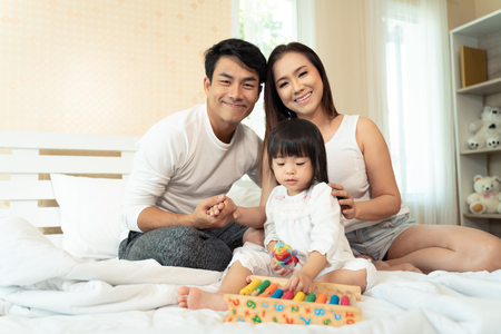 Happy family playing toys with daughter in bed at home.の写真素材