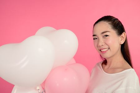 woman in white dress with balloon heart shape isolated on pink backgroundの写真素材