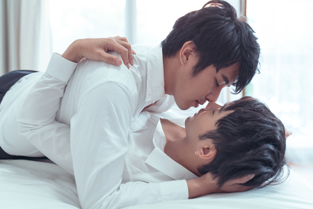 Gay couple spending time in bed and takecare hugging and kissing together.の写真素材