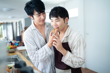 Sweet gay couple preparing a meal in kitchen at homeの写真素材