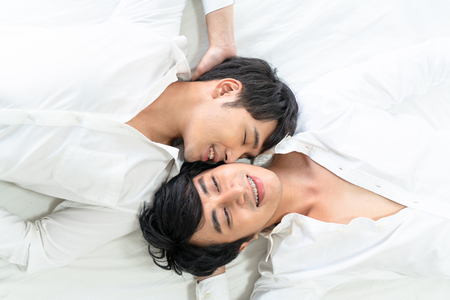 Gay couple spending time in bed and takecare hugging and kissing together.の写真素材