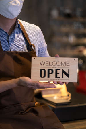 Coffee shop owner with face mask holding holding open sign after lock down and re-open again.の写真素材