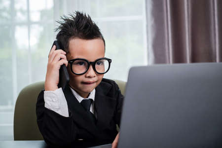 Litte Boy in business suit working with notebook and calling mobile in office.の写真素材