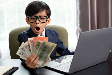 Little boy in Business suit working with notebook and holding international banknote. Success in his business.の写真素材