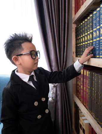 Little boys in suit looking and choose book in shelf.の写真素材