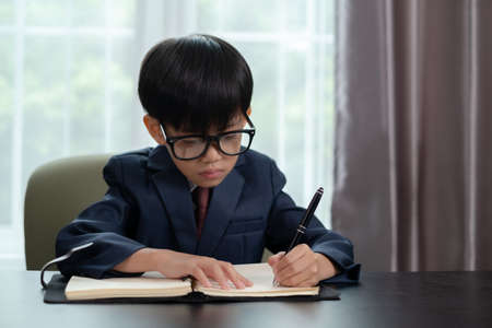 Little boy in business suit write someting on the book in office.の写真素材