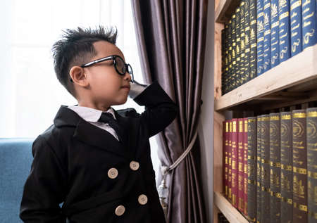 Little boys in suit looking and choose book in shelf.の写真素材