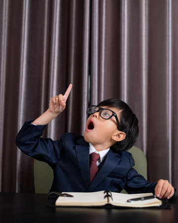 Little boy in business suit write someting on the book and pointing on top blank space.の写真素材