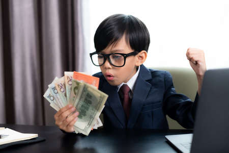 Little boy in Business suit working with notebook and holding international banknote. Success in his business.の写真素材