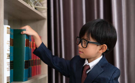 Little boys in suit looking and choose book in shelf.の写真素材