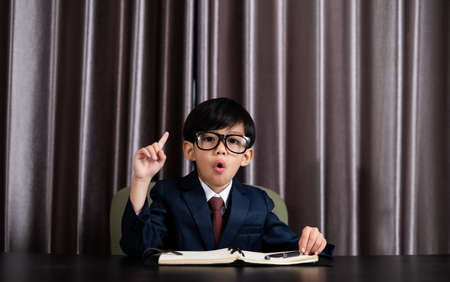 Little boy in business suit write someting on the book and pointing on top blank space.の写真素材