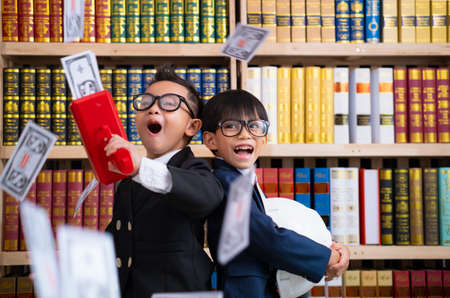 Little boys in suits use the cash cannon with money and Another boy holding engineer hat.の写真素材